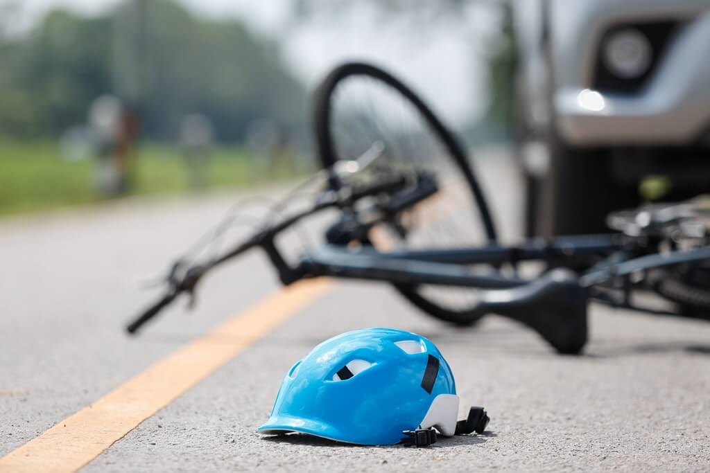 bicycle and cyclist helmet on the road with a car visible behind them